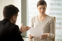 Woman in meeting holding document and looking skeptically at her manager.